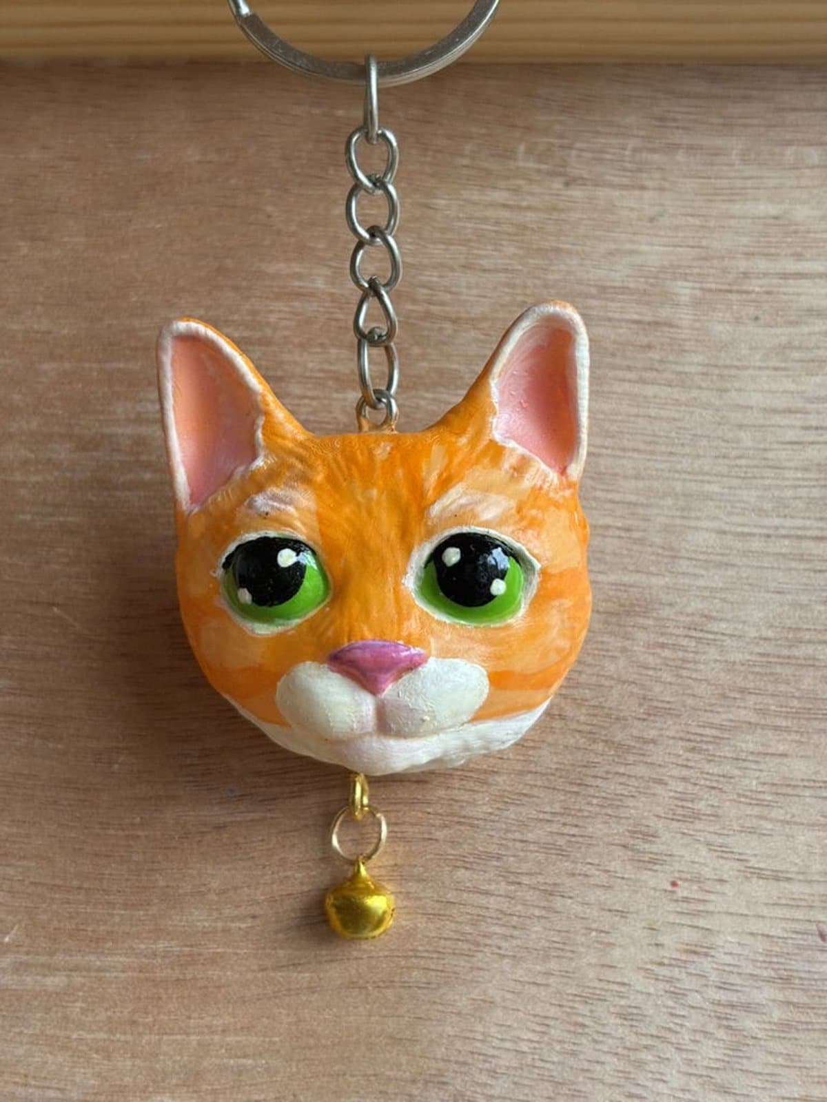Llavero de gatito naranjo de ojos verdes con cascabel dorado.