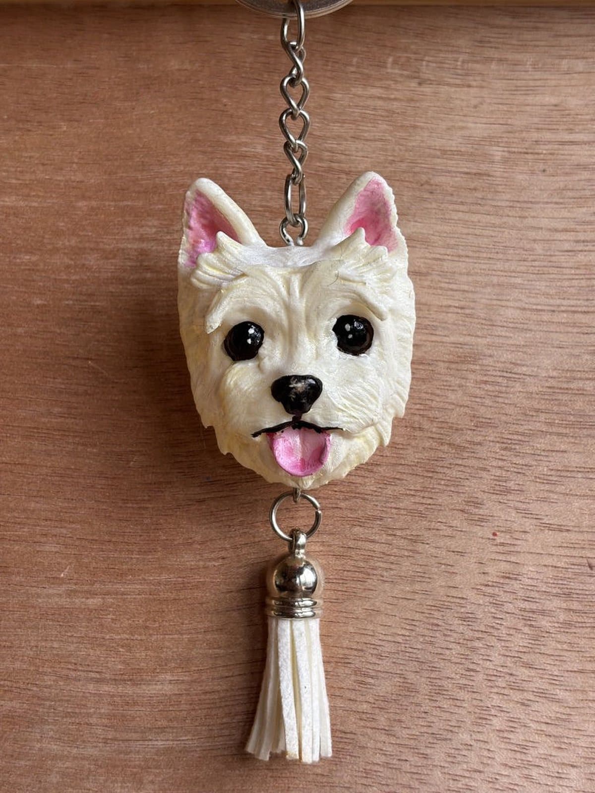 Llavero pintado a mano de un westie blanco con la lengua afuera, orejas rosadas y borla blanca.