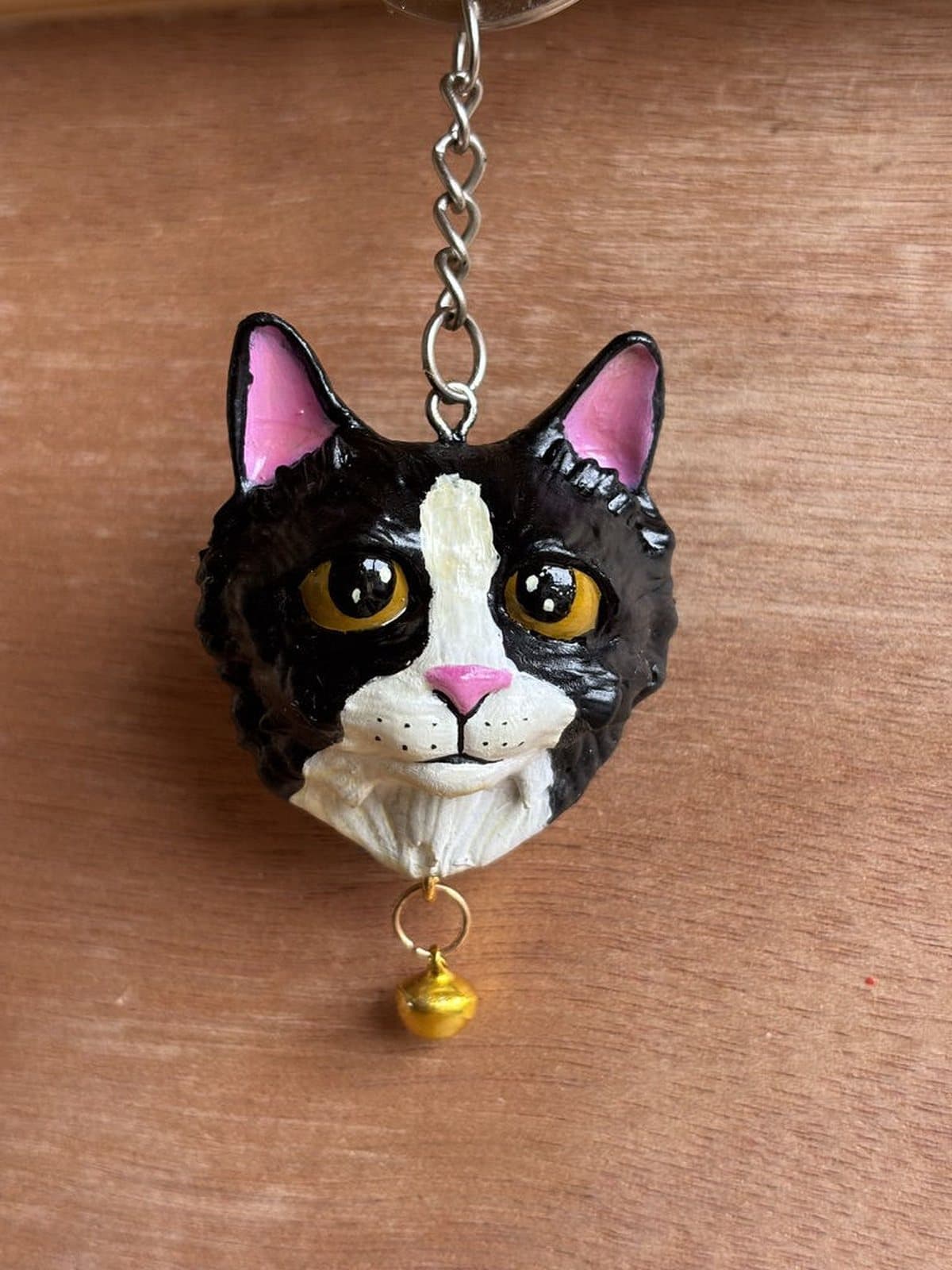 Llavero pintado a mano de un gato negro y blanco de pelaje largo, con cascabel dorado.