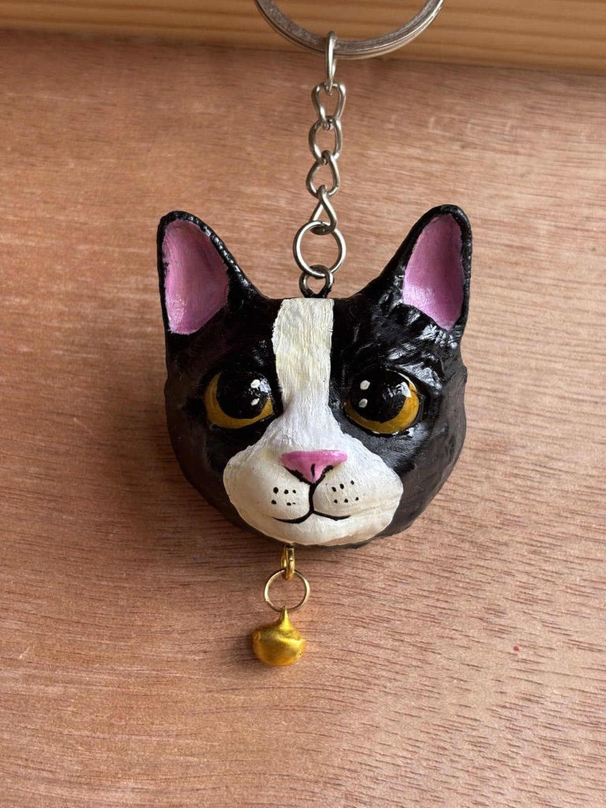 Llavero pintado a mano de un gato negro con una franja blanca y ojos ámbar, con cascabel dorado.