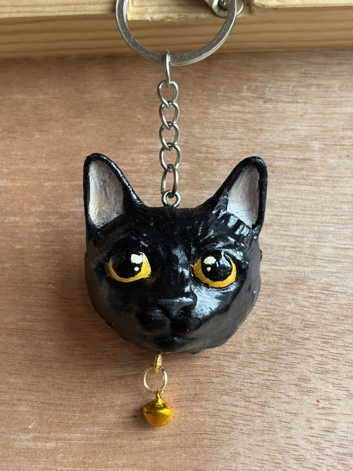 Llavero pintado a mano de un gato negro de ojos amarillos, con cascabel dorado.