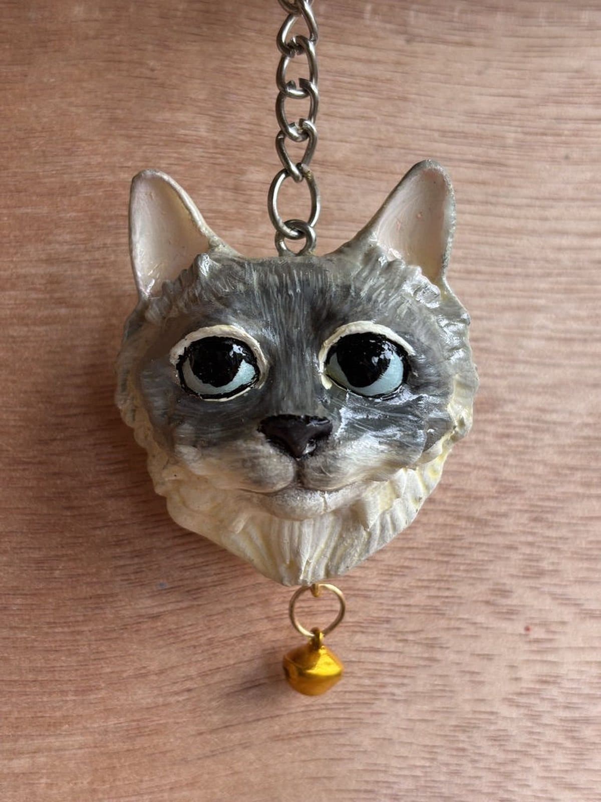 Llavero pintado a mano de un gato gris claro de ojos grandes, con cascabel dorado.