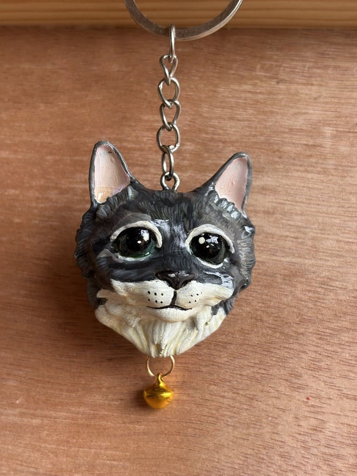 Llavero pintado a mano de un gato gris atigrado de ojos verdes, con cascabel dorado.