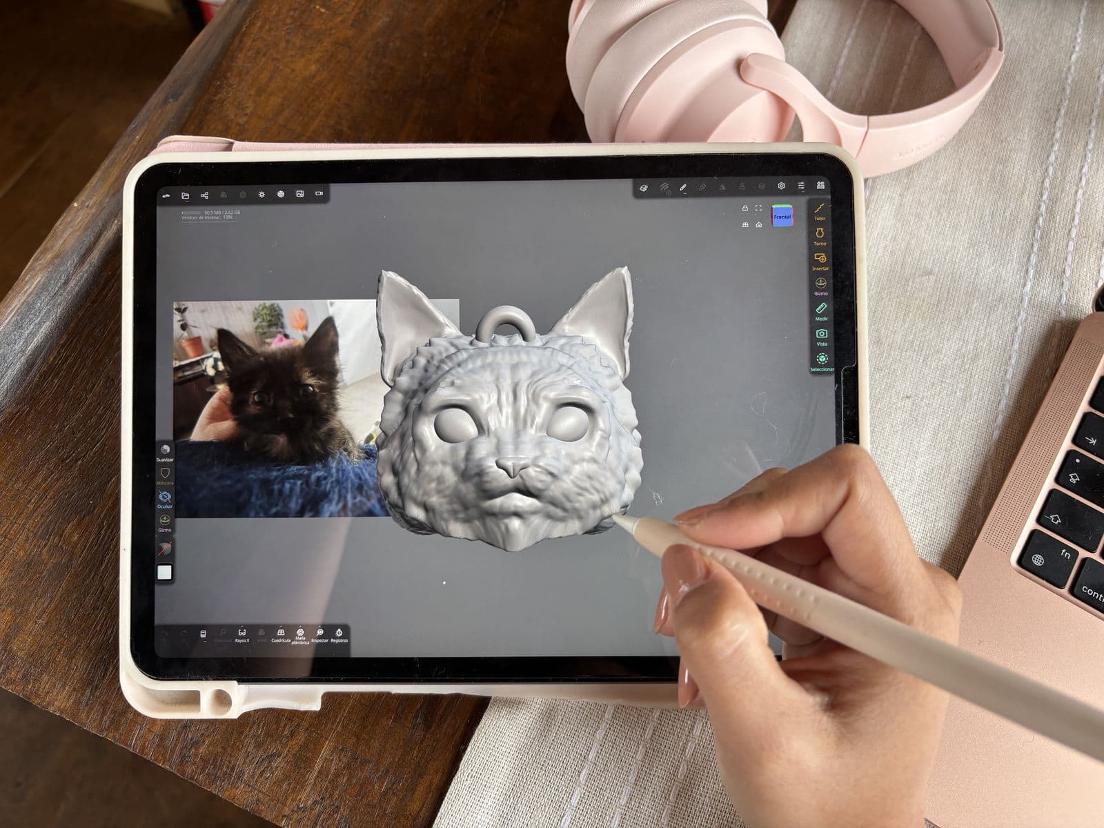 La mano de Catalina esculpe con lápiz digital, en una tablet, la cabeza 3D de un gato a partir de la fotografía de un gatito oscuro.